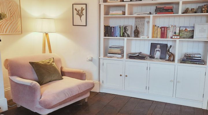 Cozy up in this charming Warminster living room, featuring a plush pink chair, stylish bookshelf, and warm lamp lighting.